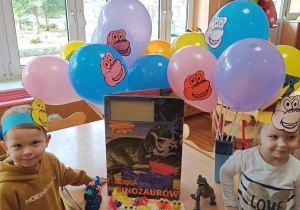 Chłopiec i dziewczynka w opaskach na głowie z rysunkami dinozaurów.
